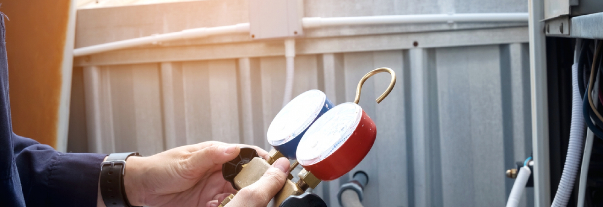 Technician holding two pressure gauges while working on an AC Unit