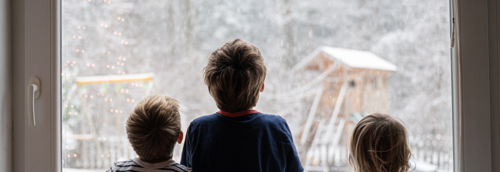 three children at a window looking at the snow outside