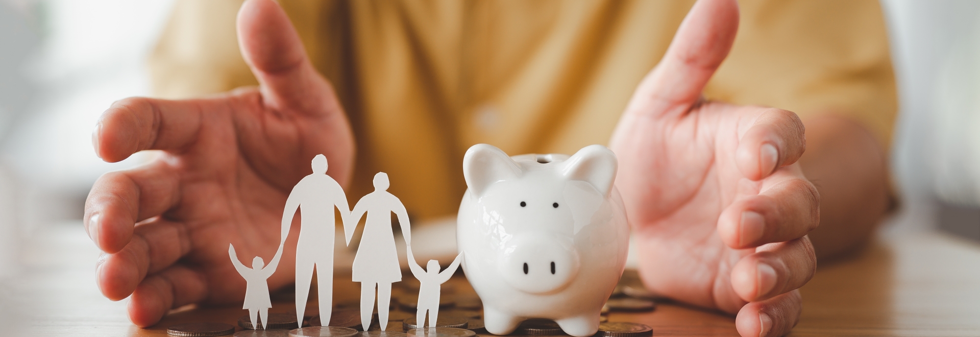 person holding a piggy bank and a family cut out of paper