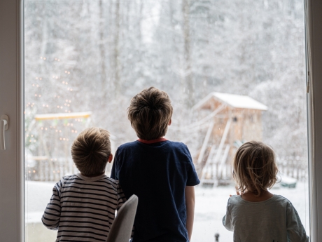 three children at a window looking at the snow outside